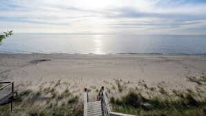 A beach with a wooden walkway leading to the water, a clear sky, and calm sea.