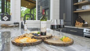 A kitchen with a marble countertop, a bottle of wine, glasses, and a variety of cheeses and fruits. - Back Deck with a View - Games - Pets - Hickory Pines (Broken Bow)