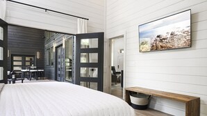 A modern bedroom with a large bed, a wooden bench, and a painting of a rocky landscape. - Back Deck with a View - Games - Pets - Hickory Pines (Broken Bow)