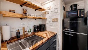 Une cuisine avec des étagères en bois, un évier en acier inoxydable, un réfrigérateur noir et un four à micro-ondes.