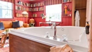 Une pièce avec une grande baignoire, des étagères en bois, un canapé et une fenêtre.