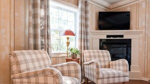 Un salon avec deux fauteuils à motifs écossais, une cheminée, un téléviseur et une lampe.