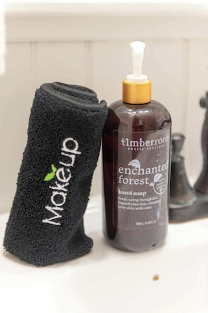 A black towel with 'Makeup' and a green leaf logo, and a bottle of 'Timberroot enchanted forest hand soap' next to it.