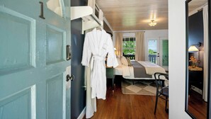 A room with a bed, a chair, a robe hanging on a rack, and a door with a number.