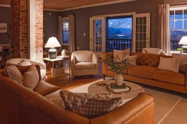 A cozy living room with a brown sofa, a beige armchair, a coffee table with a vase, and a view of the outdoors through a door.