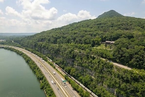 A highway adjacent to a river with a forested hill in the background.