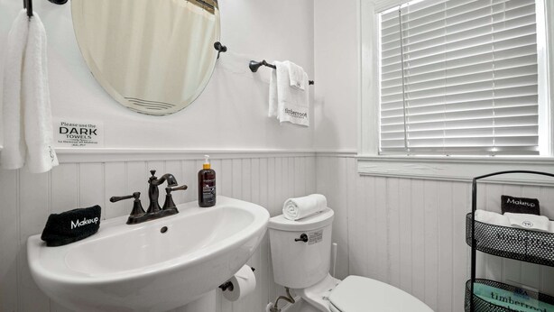 A bathroom with a white sink, toilet, and a window with blinds. - Historic Riverview Inn - King Room One (Chattanooga)