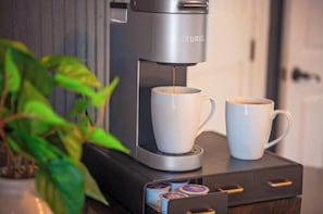 A coffee machine with two cups, a plant, and a drawer with coffee pods.