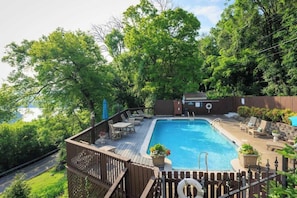 A swimming pool with a wooden deck, lounge chairs, and a small building in the background.