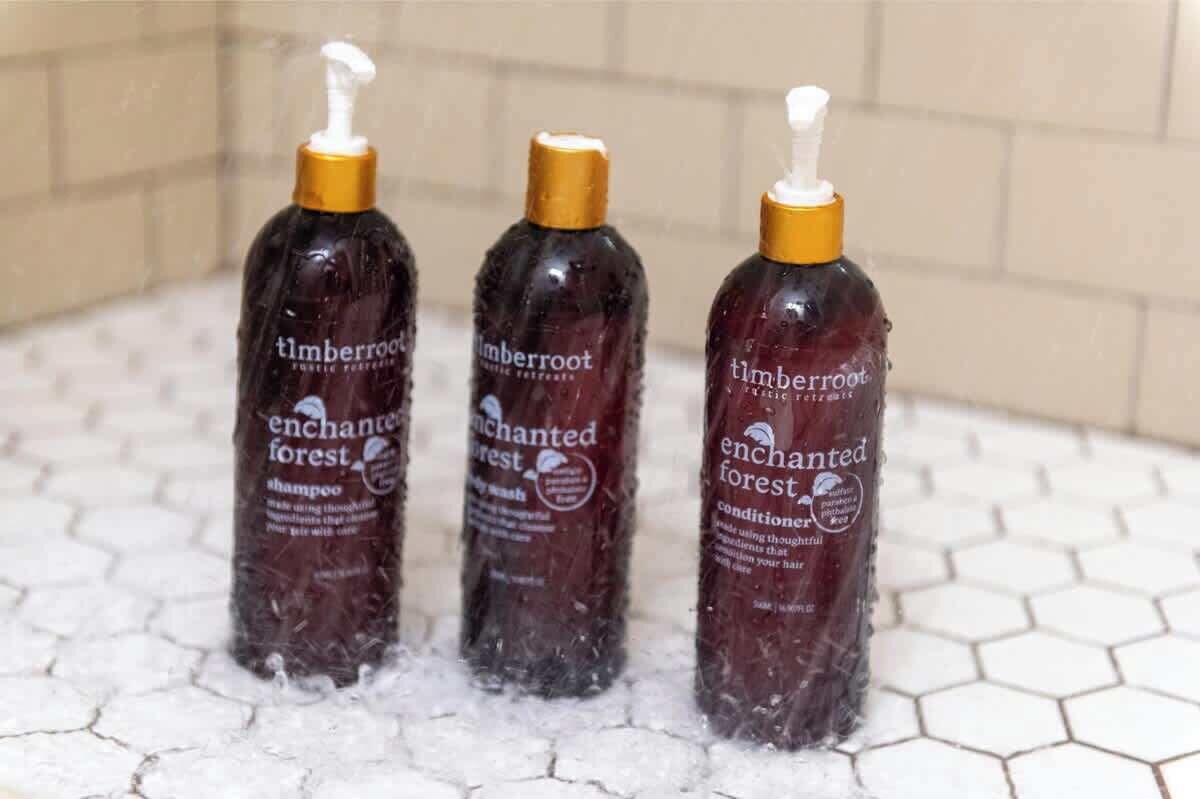 Tres botellas de champú y acondicionador Timberroot Enchanted Forest sobre una superficie de baldosas.