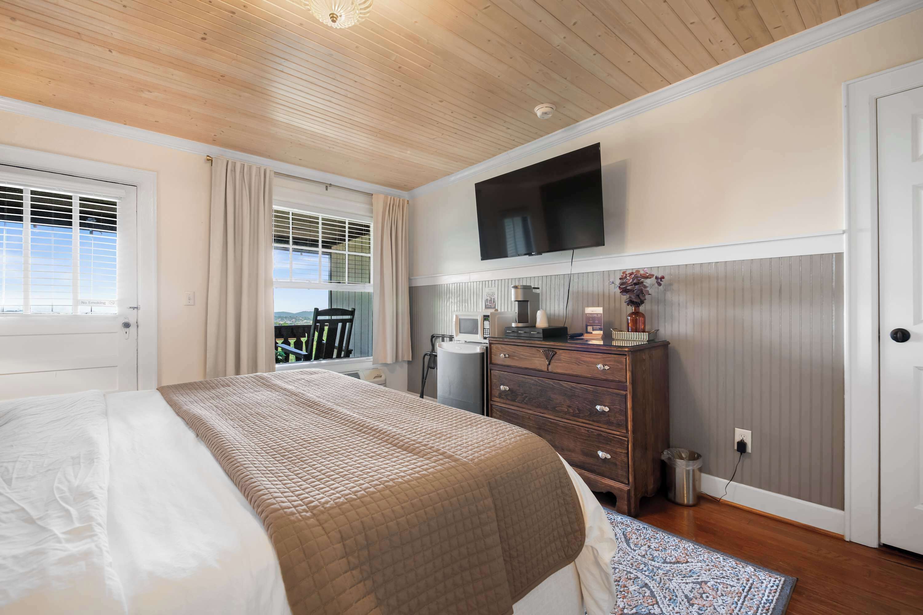 Un dormitorio con cama, cómoda, televisor y ventana con cortinas.