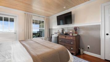Un dormitorio con cama, cómoda, televisor y ventana con cortinas.