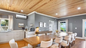 A modern kitchen with a wooden ceiling, a dining area with a large wooden table and white chairs, and a gray wall with framed pictures. - Historic Riverview Inn - King Room Seven (Chattanooga)