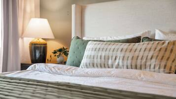 A neatly made bed with a striped pillow, a lamp, and a plant on a bedside table.