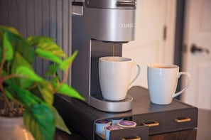 A coffee machine with two cups, a plant, and a drawer with coffee pods.