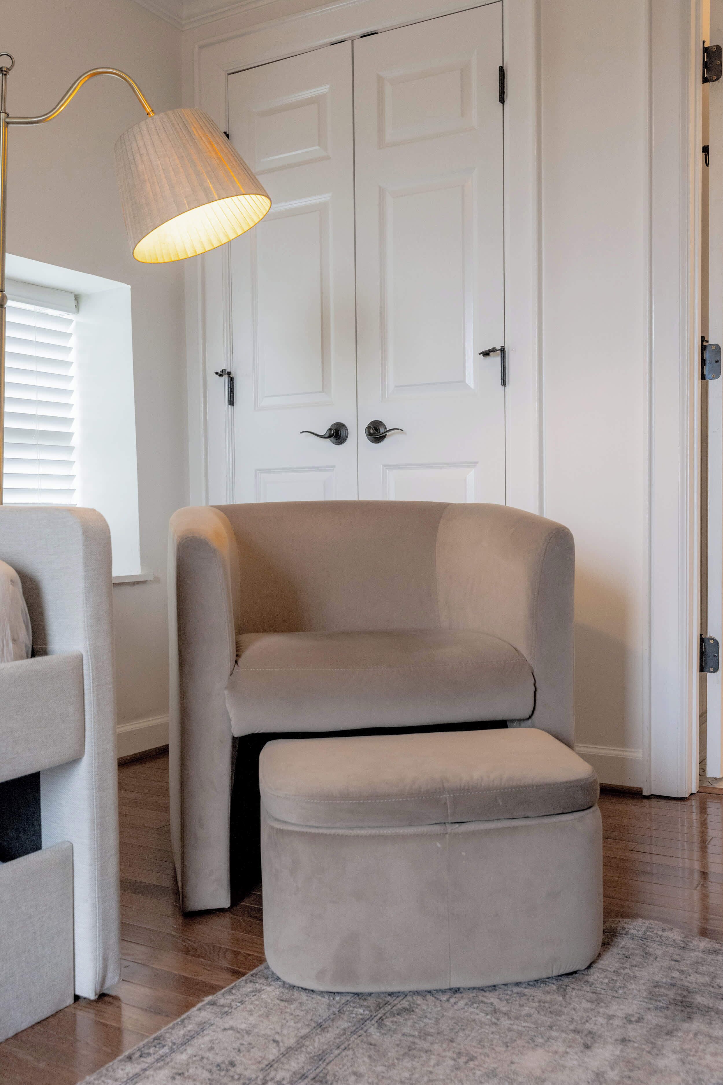 A room with a beige armchair, a matching ottoman, a floor lamp, and a white door.
