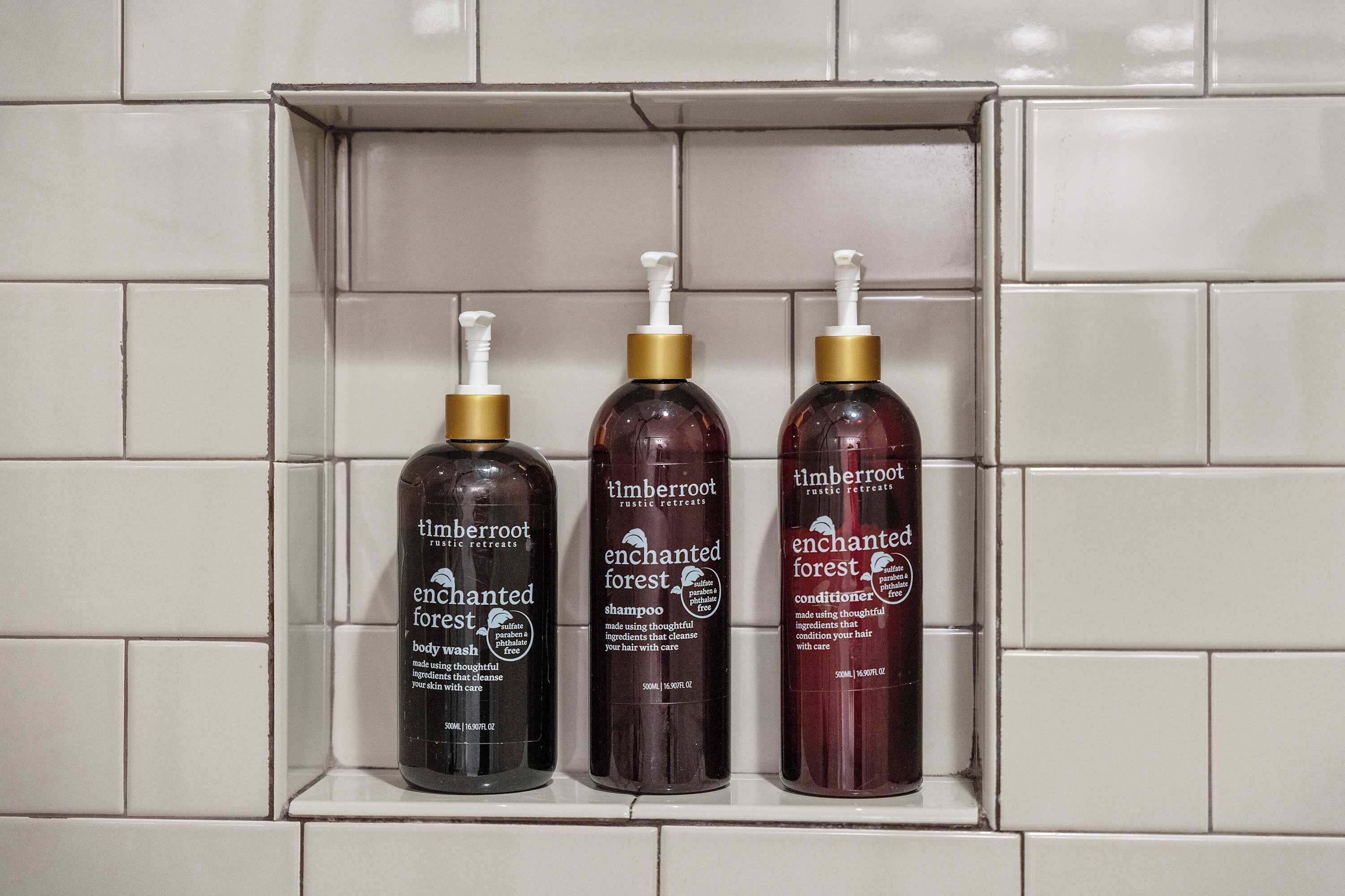Drie flessen Timberroot Enchanted Forest douchegel en conditioner op een betegeld schap.