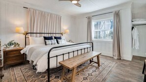 A bedroom with a bed, bedside lamps, a wooden bench, a patterned rug, a ceiling fan, and a window with curtains. - Lookout Mountain Cottage (Lookout Mountain)
