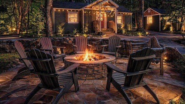 A stone fire pit with chairs, a wooden deck, and a house with string lights. - Lookout Mountain Cottage (Lookout Mountain)
