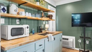 Une cuisine équipée d’un four à micro-ondes, d’un évier, d’étagères en bois et d’un téléviseur.