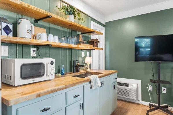 Une cuisine équipée d’un four à micro-ondes, d’un évier, d’étagères en bois et d’un téléviseur.