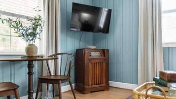 A room with a wooden table, a chair, a vintage radio, and a television mounted on the wall.