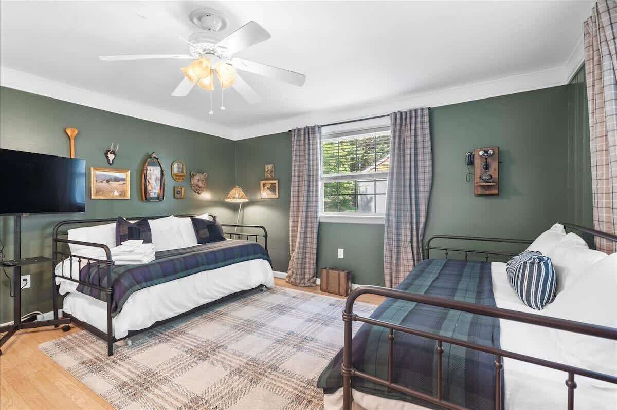 A room with two beds, a ceiling fan, a window with curtains, and wall-mounted decorations.
