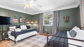 A room with two beds, a ceiling fan, a window with curtains, and wall-mounted decorations.