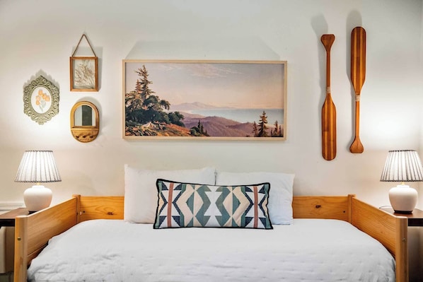 A bedroom with a bed, pillows, a painting, two wooden paddles, and a mirror.