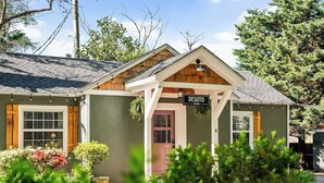 Una cabaña de dos pisos con un porche delantero, un cartel que dice 'DESOTO COTTAGE' y un pequeño jardín.