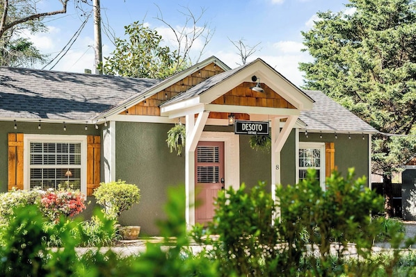 A two-story cottage with a front porch, a sign reading 'DESOTO COTTAGE,' and a small garden area.