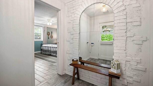 Un baño con pared de ladrillo blanco, banco de madera y espejo.