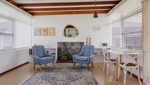 A room with two blue armchairs, a white table with chairs, a fireplace, and framed pictures on the wall. - Boardwalk Bungalow - pristine ocean views (Urunga)