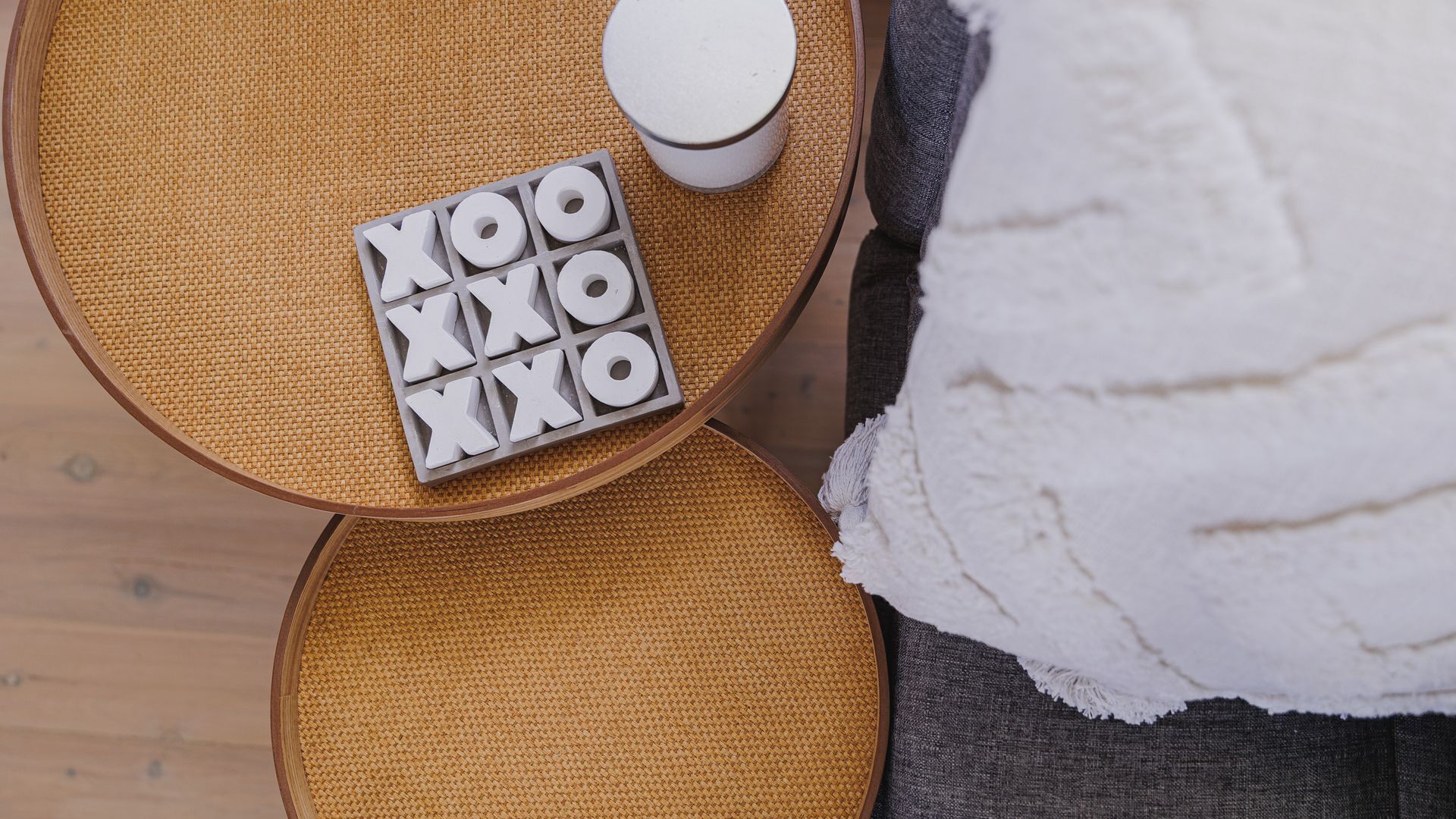 A round wooden table with a woven mat, a white container, and a tray with letter-shaped objects.