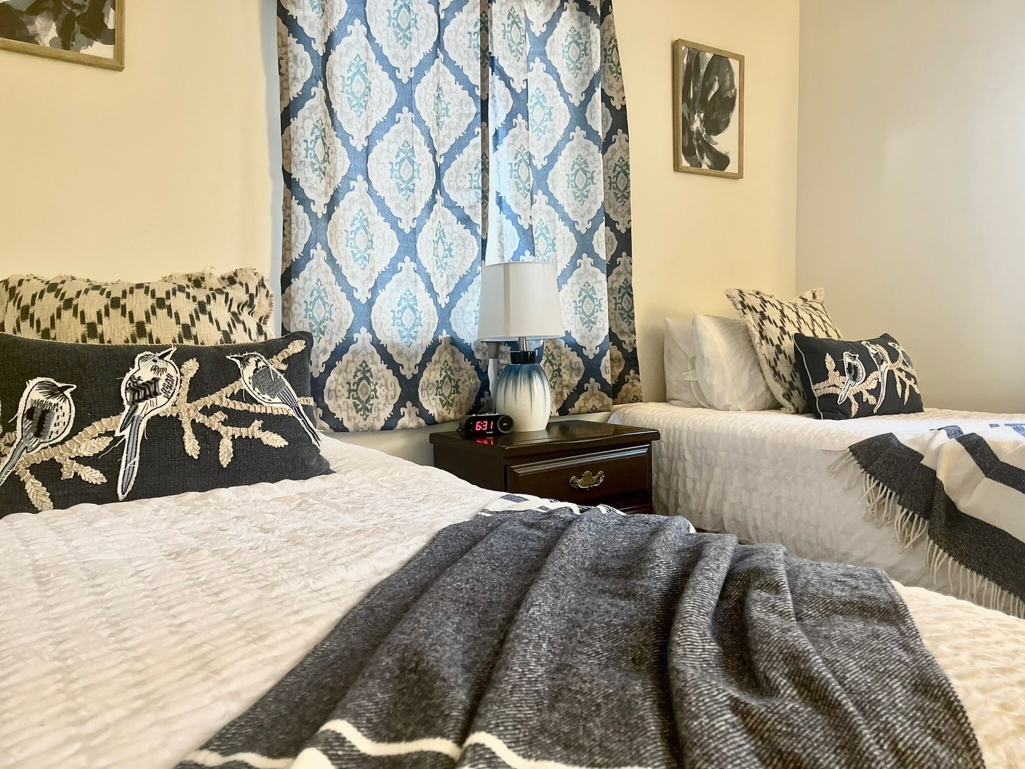 A hotel room with two beds, a nightstand with a lamp, and patterned curtains.
