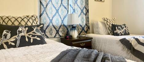 A hotel room with two beds, a nightstand with a lamp, and patterned curtains.