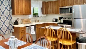 Una cocina moderna con armarios de madera, un refrigerador de acero inoxidable y un comedor con mesa lista para cuatro comensales.