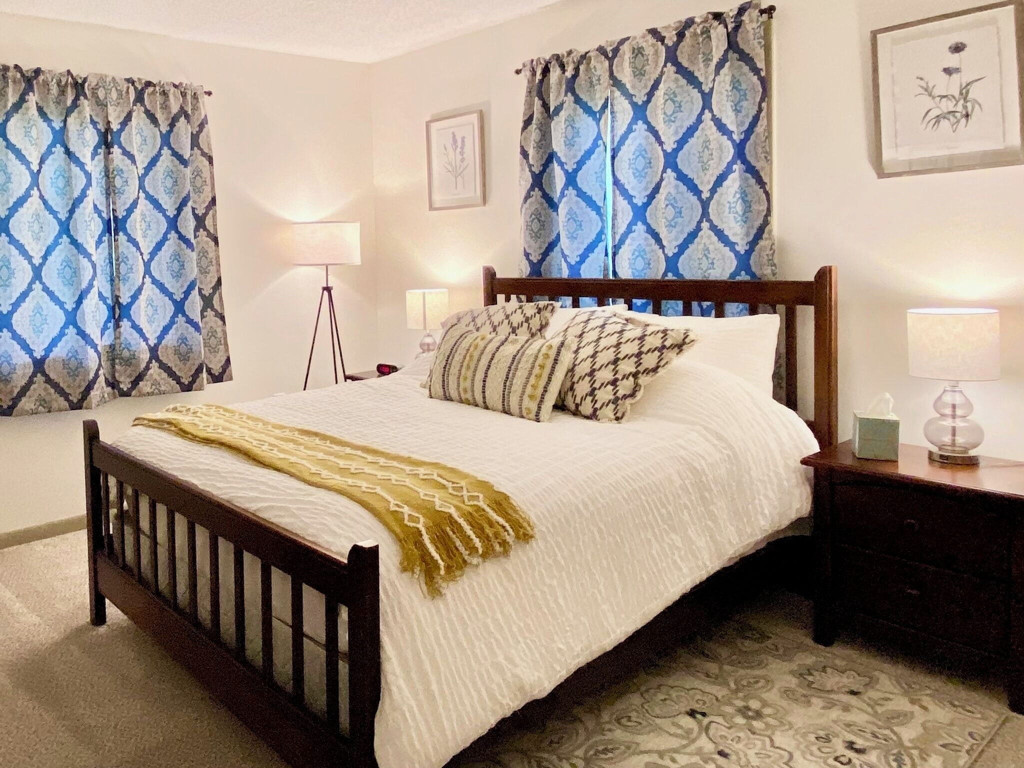 A neatly made bed with a wooden frame, two bedside lamps, and a bedside table with a tissue box.