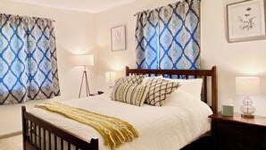 Una cama bien hecha con cabecera de madera, dos lámparas de noche y una mesita de noche con un dispensador de pañuelos.
