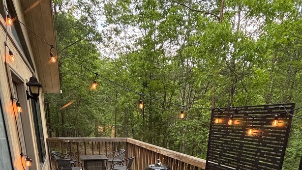 Un jacuzzi en una terraza de madera con luces de cadena, rodeado de árboles.