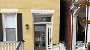 A two-story building with a yellow facade, a wooden front door, and a number "2717" above the entrance.