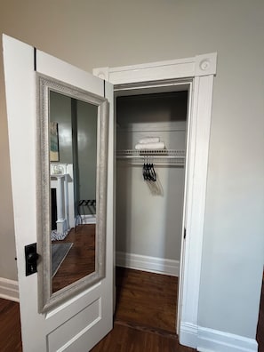 A room with a white door, a mirror, a closet with shelves, and a black chair.
