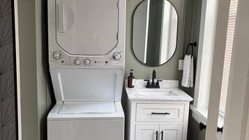 Une petite salle de bain avec un lave-linge blanc, un lavabo et un miroir.
