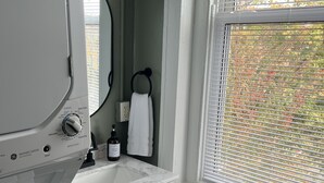 A bathroom with a white washing machine, a sink with a marble countertop, a towel ring, and a window with blinds.