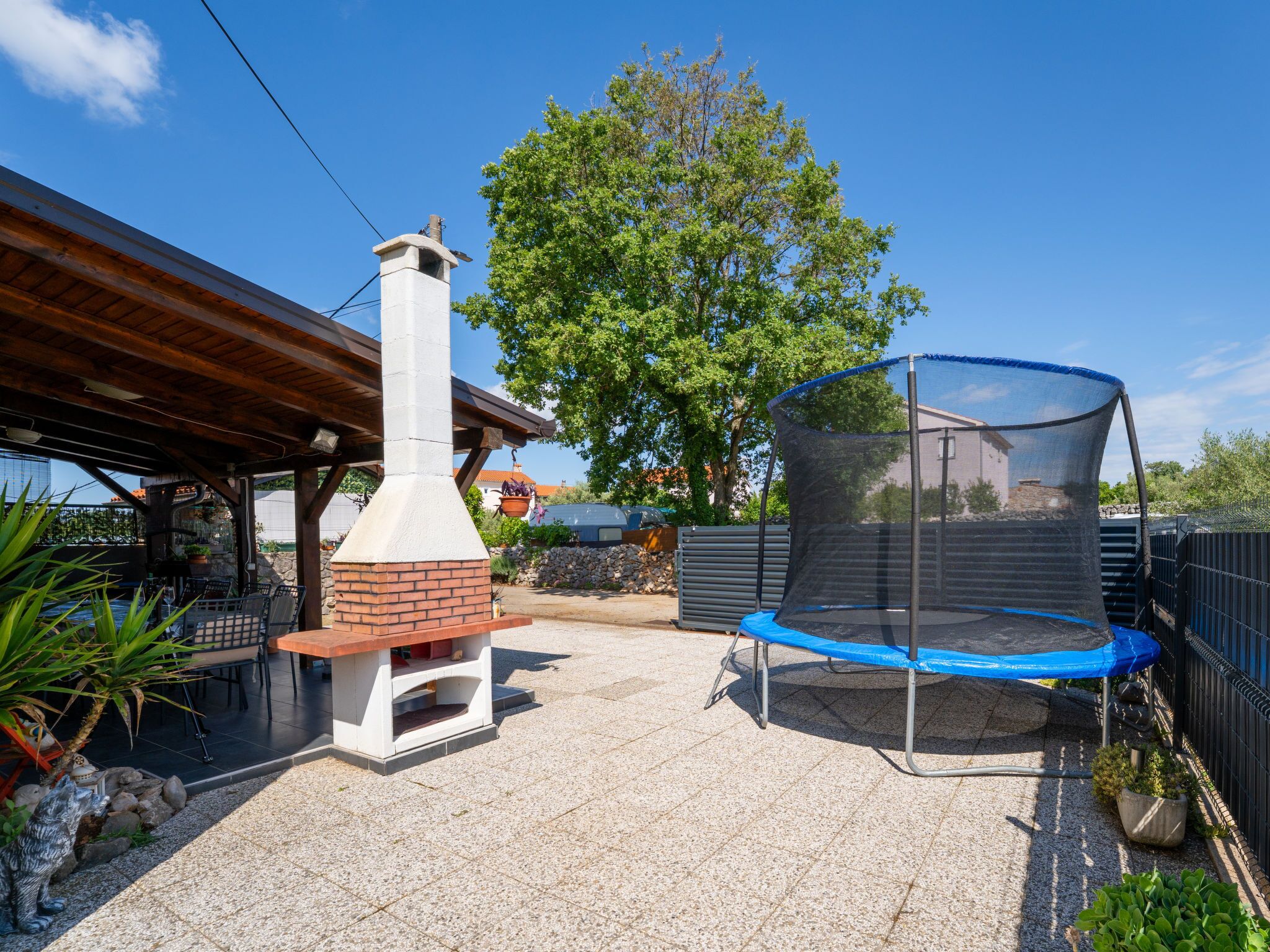 A patio with a brick oven, a trampoline, and a covered seating area.