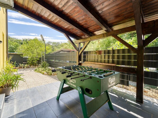 An outdoor patio area with a foosball table, wooden beams, and a covered section.