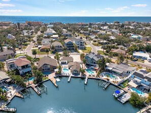 An aerial view of a coastal residential area with a marina, houses, and a large swimming pool. - IRB Oasis: 2 homes, Heated Salt Pool, Waterfront, Sleeps 14 (Indian Rocks Beach)