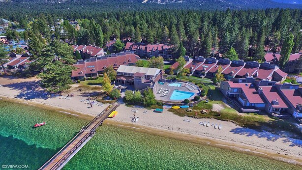 Vista aérea de una zona residencial costera con casas, una playa y una piscina azul cristalina.