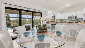 A modern kitchen with white cabinets, a built-in microwave, and a dining area with a glass table and white chairs. - Tropical Oasis, Heated Pool & Spa, Bikes - Villa 7 Palms - Roelens (Cape Coral)