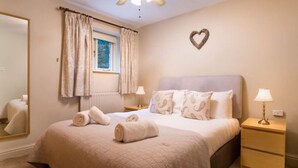 A neatly made bed with rolled towels, a bedside lamp, and a heart-shaped decoration on the wall. - Thomas Fold Flat - Ambleside - perfect for couples (Ambleside)